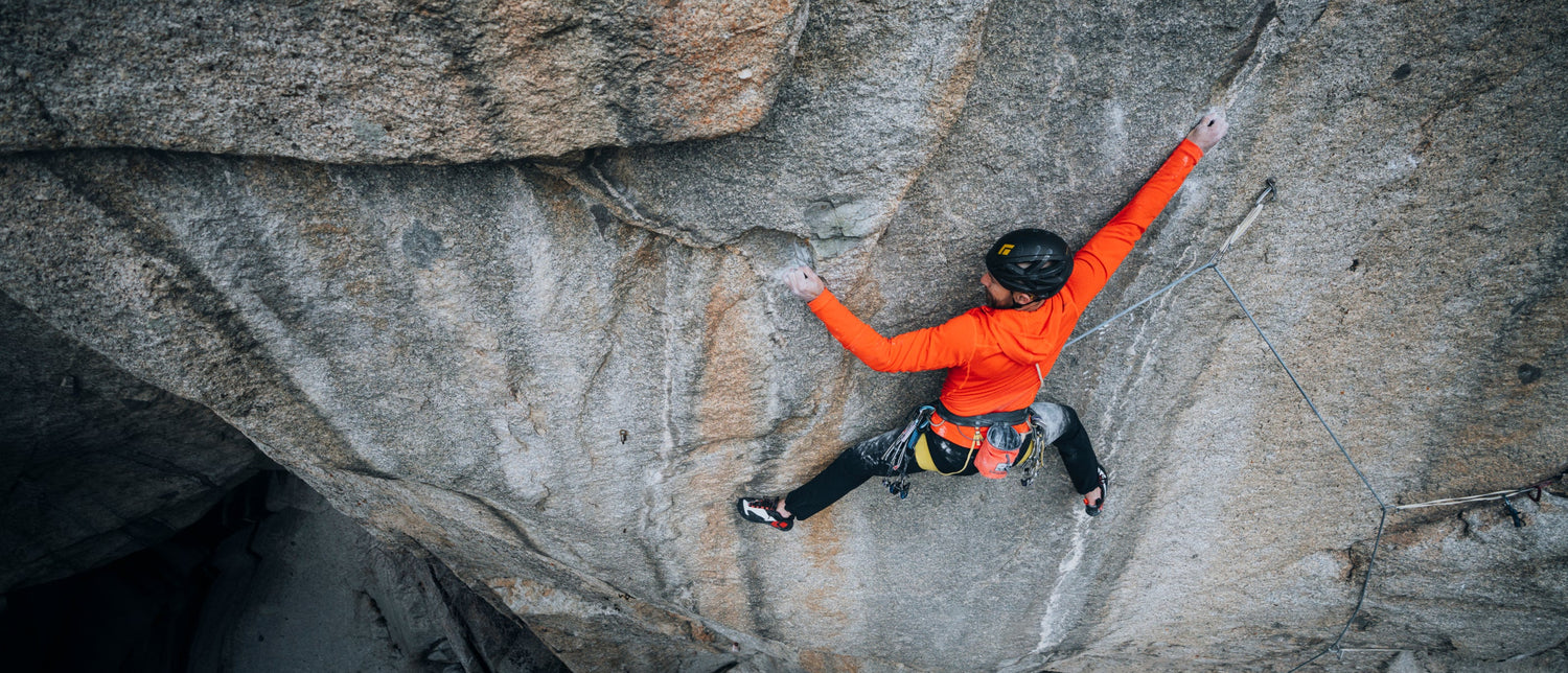 A climber reaches across a blank granite face. 