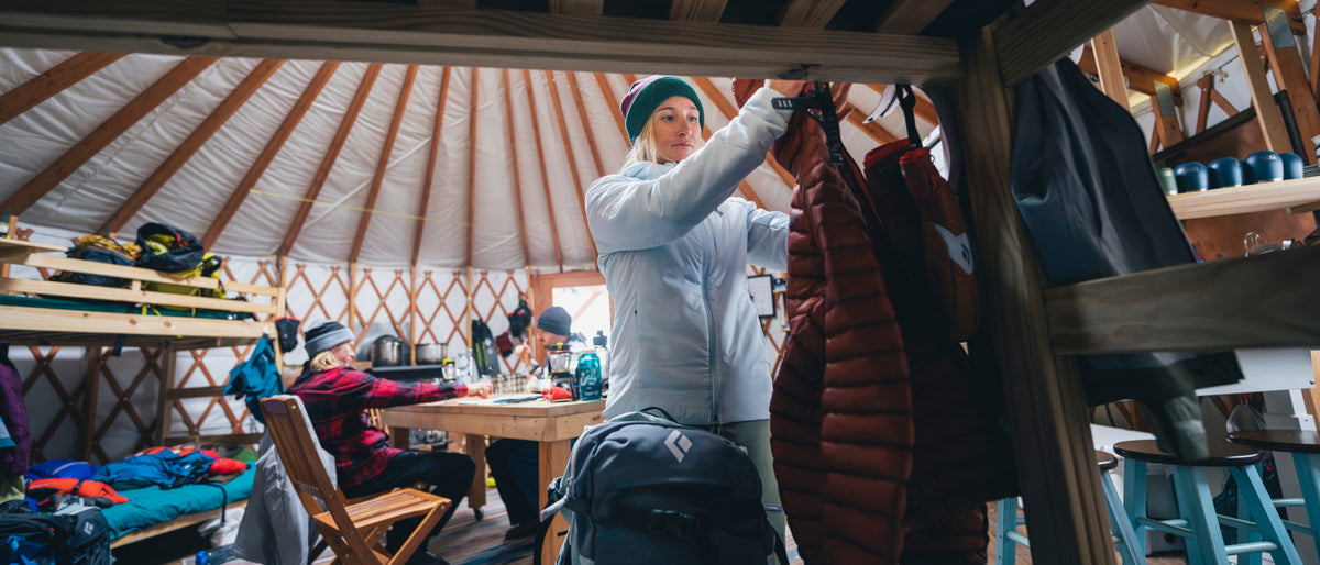 In a yurt, a skier adjusts the touring gear by the bunkbed. 
