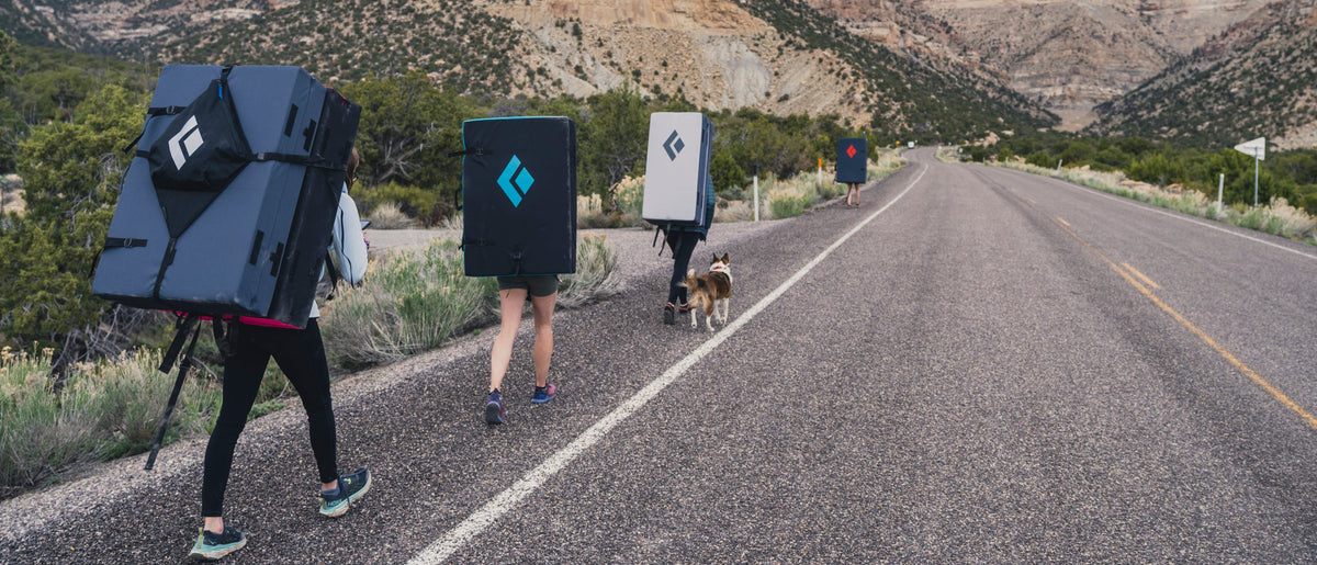 Four boulderers with bouldering pads on their back walk on the road to some problems. 