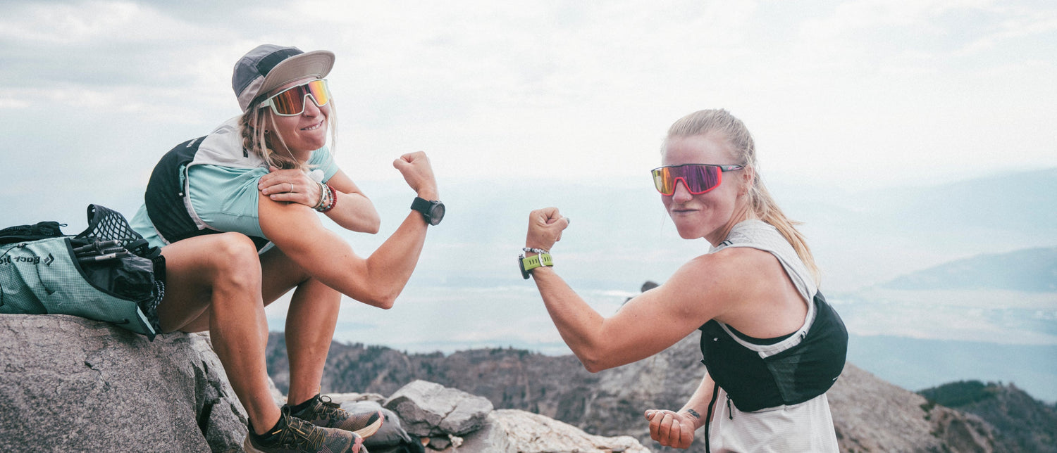 Two runners flex at the top of a ridge, celebrating their climb. 