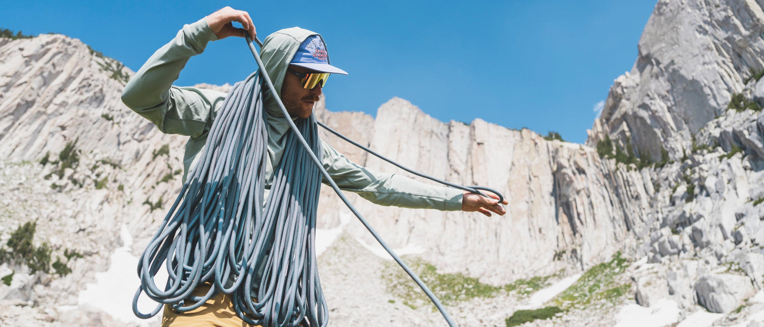 After a climb, a climber coils a rope over their shoulders with granite walls in the background. 