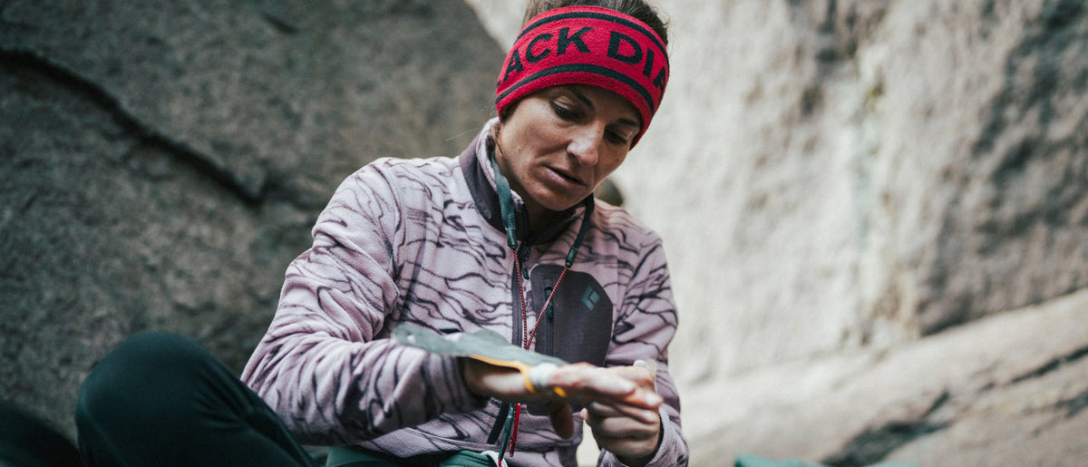 A climber puts on crack gloves at the crag while wearing a pink Black Diamond fleece. 