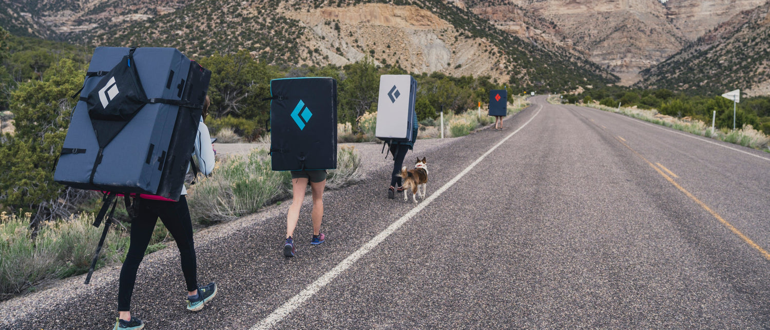 Three climbers head to the project with bouldering pads. 