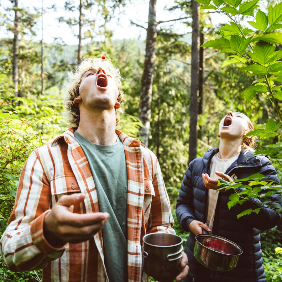 A hiker wearing a project flannel tosses a berry into their mouth. 
